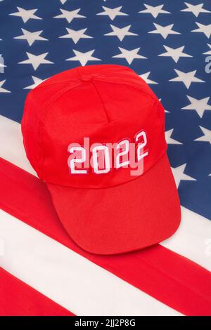 Rote MAGA-Kappe mit Datum 2022 und US Stars and Stripes-Flagge. Für die US-Zwischenwahlen vom 2022. November und die Ausrottung der Demokraten durch die US-Republikaner der Roten Welle. Stockfoto