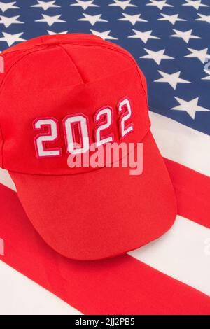 Rote MAGA-Kappe mit Datum 2022 und US Stars and Stripes-Flagge. Für die US-Zwischenwahlen vom 2022. November und die Ausrottung der Demokraten durch die US-Republikaner der Roten Welle. Stockfoto