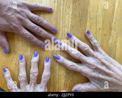 Ältere Großmutter und Enkel maniküren und polieren ihre Nägel zusammen mit einer violetten Farbe Stockfoto