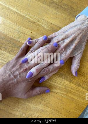 Ältere Großmutter und Enkel maniküren und polieren ihre Nägel zusammen mit einer violetten Farbe Stockfoto