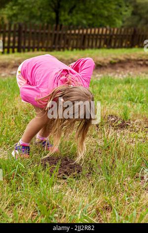 Junge, süße, weiße Frau, Kind, beugt sich nach unten, um Schlamm oder Kuh Extremitäten zu erkunden, Schimmel. Familienurlaub Stockfoto