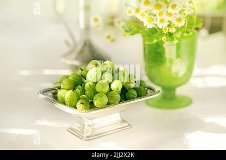 Grüne reife Stachelbeeren in einer antiken silbernen Vase auf dem Tisch. Schönes Stillleben mit Stachelbeeren und antiken Gerichten und einem natürlichen Kontrast Stockfoto