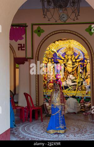 Howrah, Indien -26.. Oktober 2020 : Bengalisches Mädchen Kind posiert mit Göttin Durga im Hintergrund, im Altersheim dekoriert. Durga Puja. Stockfoto