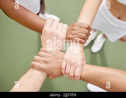 Gemeinsam können wir unsere Träume verwirklichen. Aus dem Hochwinkel vier unverkennbare Tennisspieler, die in einem Geheule auf dem Platz stehen. Stockfoto