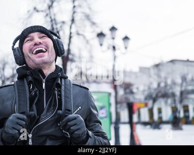Porträt eines jungen Mannes, der auf einer Straße lacht und Musik hört. Stockfoto