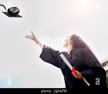 Shell gehen weit ins Leben. Low-Angle-Aufnahme einer jungen Frau, die ihren Hut am Abschlusstag in die Luft wirft. Stockfoto