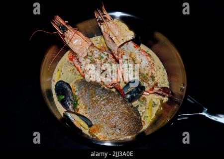 Verschiedene Meeresfrüchte-Rezepte, in der Pfanne angebratener Seebarsch, gegrillte Garnelen, Muscheln in cremiger Weißweinsauce Stockfoto