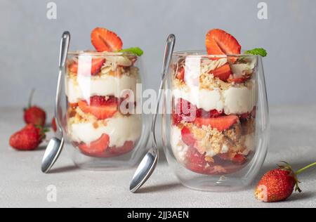 Erdbeerdessert in Gläsern mit Keks, Mascarpone-Käse und Mandeln. Köstliches Dessert für Kinderparty auf hellgrauem Hintergrund Stockfoto