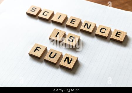 ​ Holzbuchstaben buchstabieren „Wissenschaft macht Spaß“ auf einem weißen, weißen Notizblock. Schreibtischoberfläche aus Hartholz. Zurück in die Schule, persönlich lernen. Stockfoto
