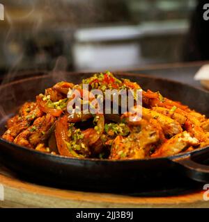 mexikanisches Essen, Hühnerfajitas auf einem heißen, rauchenden, brutzelnden Teller in Nahaufnahme Stockfoto