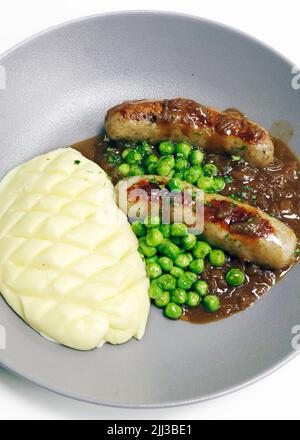 Knaller und Maische, britische Delikatesse, Schweinewürste, Kartoffelpüree, grüne Erbsen und Zwiebelsoße Stockfoto