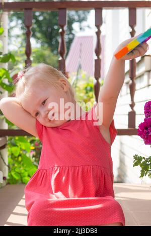 Nette kaukasische faires Haar Mädchen in rosa Kleid spielt und zeigt lustige trendige Silikon Antistress bunte Spielzeug popit. Push Popper Fidget Spielzeug ist die Stockfoto