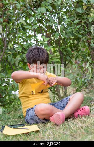 Junge spielen werfen Papier Flugzeug im Freien suchen weg. Portrait eines fröhlichen kaukasischen Jungen, der im Frühling und Sommer Park spielt und Spaß auf dem hat Stockfoto