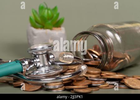 Das Konzept von Wirtschaft und Medizin kostet Gesundheit. Stapel von echten Münzen und Stethoskop. Wirtschaftliche Gesundheit isoliert auf grünem Hintergrund. Stockfoto