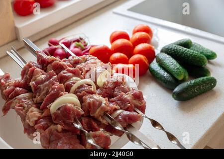 Schmackhafte, appetitliche rohe Fleischspieße im modernen Küchenhintergrund. Vresh Gemüse liegt auf dem Tisch. Stockfoto