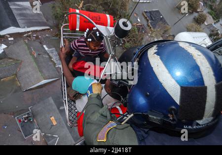 Steven Huerta bringt am 29. August 2005 in New Orleans, Louisiana, zwei Kinder in einen Rettungshubschrauber der Küstenwache. Andere beobachten von unten, wie die Kinder zu vielen Bürgern gehören, die aufgrund der Überschwemmungen von ihren Dächern gerettet werden müssen. Stockfoto