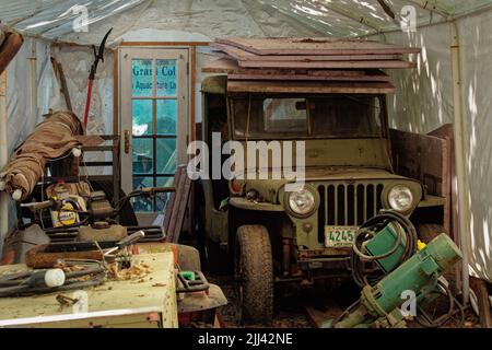 Im Essex Shipbuilding Museum Essex befindet sich ein alter, in olivfarbener Farbe lackierter Jeep in einem mit Kunststoff überzogenen Schuppen, auf dessen Dach Baumaterialien gestapelt sind. Stockfoto