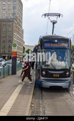 Leipzig, Deutschland - 25. Juni 2022: Leipziger Straßenbahn an der Haltestelle Augustusplatz. Die Straßenbahn in den Farben Blau und Gelb hält an einer Straßenbahnhaltestelle. Die Leute kommen auf Stockfoto