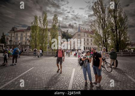 Bild von Menschen, die während eines sonnigen Sommers nach Ljubljana auf der Tromostovje-Brücke (Dreifachbrücke) zwischen dem Presernov-Platz und dem älteren Teil von Ljubljana wandern Stockfoto