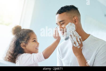 Lassen Sie mich Ihnen dabei helfen. Ein kleines Mädchen und ihr Vater spielen mit Rasiercreme in einem Badezimmer zu Hause herum. Stockfoto