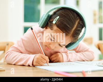 Musik und Hausaufgaben. Ein entzückendes kleines Mädchen, das Musik hört, während sie ihre Hausaufgaben macht. Stockfoto