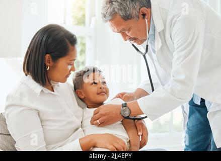 Folgen Sie der Stimme Ihres Herzens. Ein reifer Arzt hört einem kleinen Jungen beim Herzschlag während einer Untersuchung zu Hause zu. Stockfoto