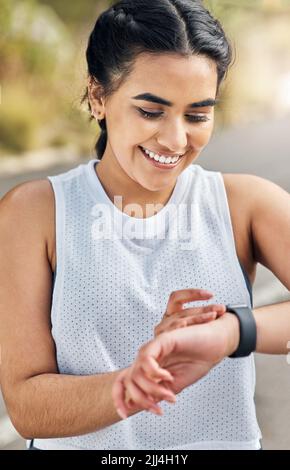 Ich bin glücklich damit. Eine junge Frau schaut auf ihre Uhr, während sie auf einen Lauf geht. Stockfoto