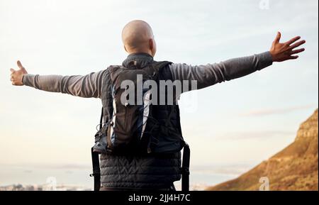 Was es bedeutet, frei zu sein. Rückansicht eines nicht erkennbaren jungen Mannes, der die Aussicht während seiner Wanderung in den Bergen genießt. Stockfoto