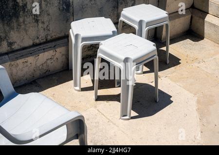 Eine Gruppe von alten Plastikstühlen, die auf einer Terrasse aus Stein verlassen wurden Stockfoto