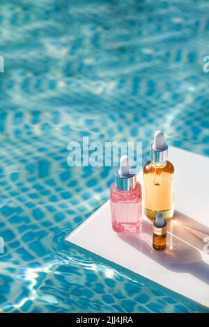 Verschiedene Verpackungen von Kosmetikbräunungsöl auf dem Hintergrund von blauem Wasser am sonnigen Sommertag Stockfoto