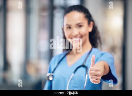 Immer positiv bleiben. Eine junge Ärztin zeigt einen Daumen nach oben in einem Krankenhaus. Stockfoto