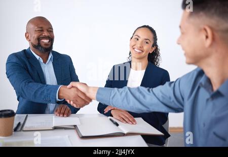 Ein Team aus lächelnden Geschäftsleuten, die sich im Büro nach einem Meeting im Sitzungssaal die Hände schütteln. Gruppe von glücklichen Profis und Kollegen mit Stockfoto