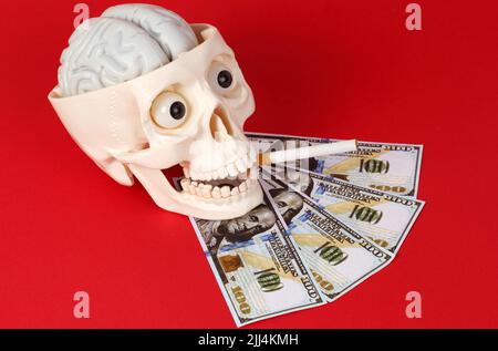 Medizin und Wissenschaft Konzept. Auf rotem Hintergrund ein Totenkopf mit einer Zigarette im Mund, in der Nähe des Geldes Stockfoto