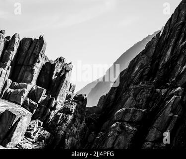 Gekippte Felsschichten der Tsitsikamma-Küste, Südafrika, mit den entfernten blauen Klippen im Hintergrund. Stockfoto