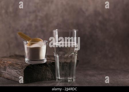 Glas mit in Wasser gelöstem Kollagen und Kollagenproteinpulver auf braunem Hintergrund Stockfoto