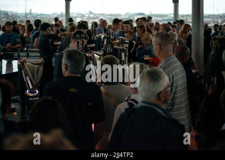 Dunkel und launisch in der Gravity Bar im Guinness Storehouse, Dublin, Irland. Gäste, die sich an der geschäftigen Bar mit Guinness Stout herumbewegen. Trinkkonzept. Stockfoto