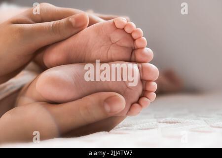 Mutter hält Babyfüße in den Händen. Beine Neugeborene in der Hand weiblicher Eltern. Kleine Kinderfüße. Nahaufnahme. Kleine Zehen des Kindes. Muttertagsurlaub Stockfoto