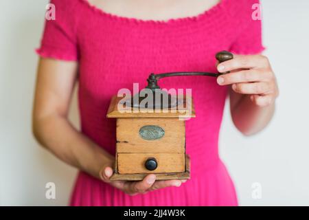 Frau in rosa Kleid hält eine manuelle Kaffeemühle in den Händen. Stockfoto