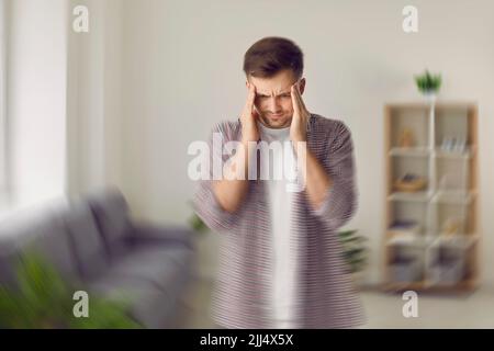 Der junge Mann spürt plötzliche Schmerzen, Schwindel und Schwindelgefühl im Kopf Stockfoto