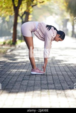 Streckt jeden Teil ihres Körpers gut aus. Eine sportliche junge Frau, die sich beim Training im Freien dehnt. Stockfoto