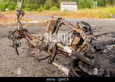 Newburn England: 16.06.2022: Gestohlenes Motorrad, das in Brand gesetzt wurde, brannte aus und wurde auf dem Industriegebiet Road mit grünen Bäumen aufgegeben Stockfoto