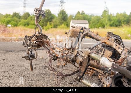 Newburn England: 16.06.2022: Gestohlenes Motorrad, das in Brand gesetzt wurde, brannte aus und wurde auf dem Industriegebiet Road mit grünen Bäumen aufgegeben Stockfoto