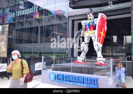 Eine Frau, die ein Mobiltelefon hält, steht vor einer großen Roboterfigur außerhalb des Siam Center, Pathumwan District, Bangkok, Thailand, Asien. Ein kleiner Junge rechts schaut auf den Roboter. Der Roboter ist dort, um für den Gundam Base Store im Siam Center zu werben. Stockfoto