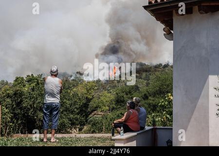 Karst, Slowenien. 22.. Juli 2022. Am sechsten Tag des Feuers beobachten die Menschen im Wald hinter einem Haus im Dorf Novelo im slowenischen Karst ein großes Waldfeuer. Etwa tausend Feuerwehrmänner mit Luftunterstützung von drei slowenischen Hubschraubern, zwei serbischen Hubschraubern, einem österreichischen Hubschrauber, einem slowakischen Black Hawk-Hubschrauber und zwei ungarischen Hubschraubern, Ein kroatisches Canadair-Löschflugzeug und ein Pilatus-Flugzeug der slowenischen Armee kämpften weiter gegen ein großes Waldfeuer, das vor fünf Tagen ausbrach und sich in der Karstregion Sloweniens verstärkt hat. Dörfer in der Umgebung waren Stockfoto