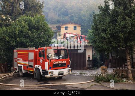 Feuerwehrautos werden vor Häusern in Vrtoce geparkt, während Feuerwehrleute ein großes Waldfeuer in den Hügeln über dem Dorf bekämpfen. Etwa tausend Feuerwehrmänner mit Luftunterstützung von drei slowenischen Hubschraubern, zwei serbischen Hubschraubern, einem österreichischen Hubschrauber, einem slowakischen Black Hawk-Hubschrauber und zwei ungarischen Hubschraubern, Ein kroatisches Canadair-Löschflugzeug und ein Pilatus-Flugzeug der slowenischen Armee kämpften weiter gegen ein großes Waldfeuer, das vor fünf Tagen ausbrach und sich in der Karstregion Sloweniens verstärkt hat. Die Dörfer in der Umgebung wurden evakuiert. Dies ist der größte Waldbrand in der Geschichte von Stockfoto