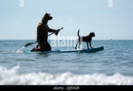 Ein Teilnehmer mit seinem Hund, der vor den Dog Masters 2022 UK Dog Surfing Championships am Branksome Dene Chine Beach in Poole, Dorset, trainiert. Bilddatum: Samstag, 23. Juli 2022. Stockfoto