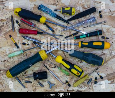 Viele Schraubendreher von kleinen bis großen Größen werden zufällig auf der osb-Bauplatte aufgeschichtet. Stockfoto