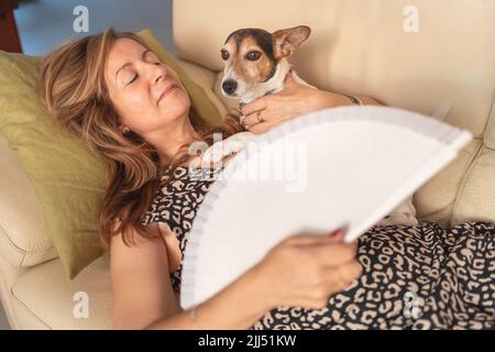 Frau, die mit ihrem Hund auf dem Sofa liegt und die hohen Temperaturen des Sommers reduziert. Stockfoto