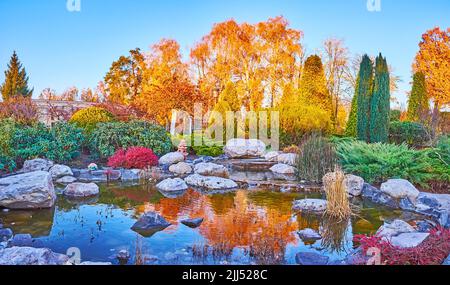 Panoramablick auf den landschaftlich schönen topiary Park mit Nadelbäumen, farbigen Büschen, leuchtend gelben Herbstbäumen und einem Teich, Mezhyhirya, Ukraine Stockfoto