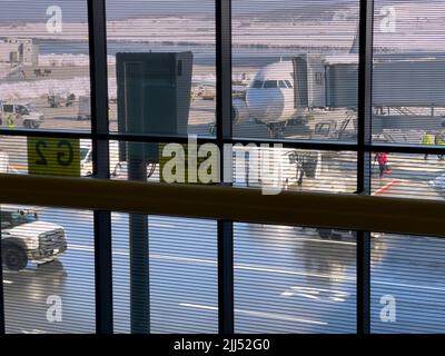 Blick durch das Flughafenfenster auf das Flugzeug, das mit der Verlängerung der Bordbrücke verbunden ist. Keine Marke. Luftfahrtkrise. Vielbeschäftigter Flugplatz. Flughafen Asphalt Stockfoto